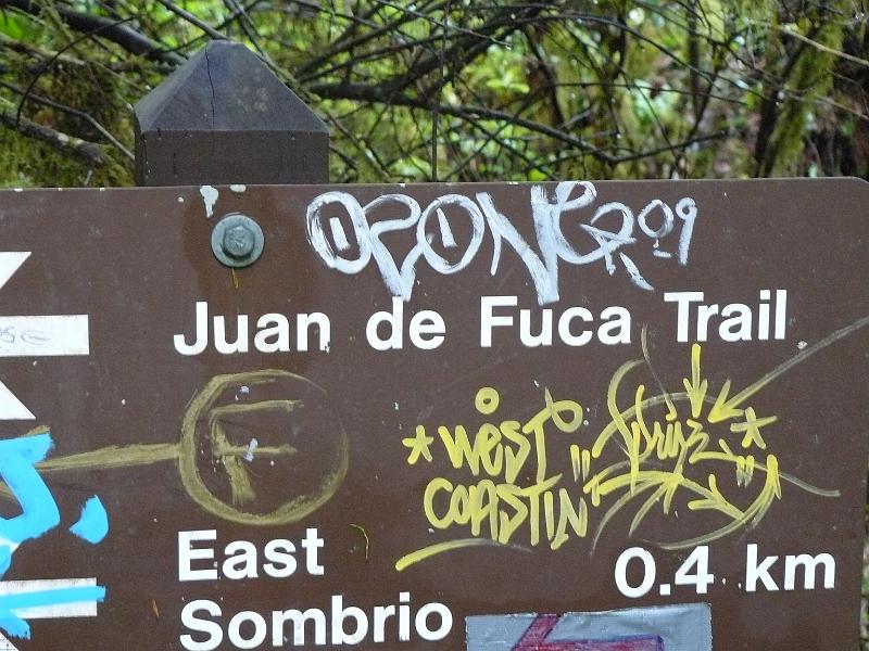 P1050838.JPG - The Juan de Fuca Trail. This was a really popular spot for surfers and since surfers are such good artists they decided to add to the sign. It was also a popular spot for car thieves apparently. There were at least three postings of cars stolen and broken into in the parking lot.